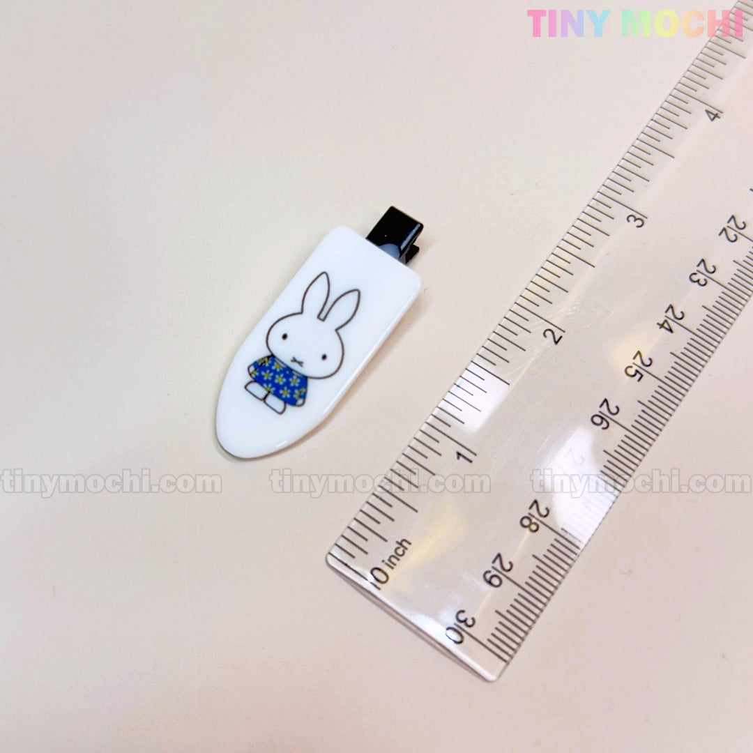 A Kawaii Bunny Hair Clip from Tiny Mochi, featuring a cute cartoon bunny in a blue sweater, rests by a clear ruler. This adorable resin alligator clip is part of the Colorful Barrette Gift Sets for Girls.