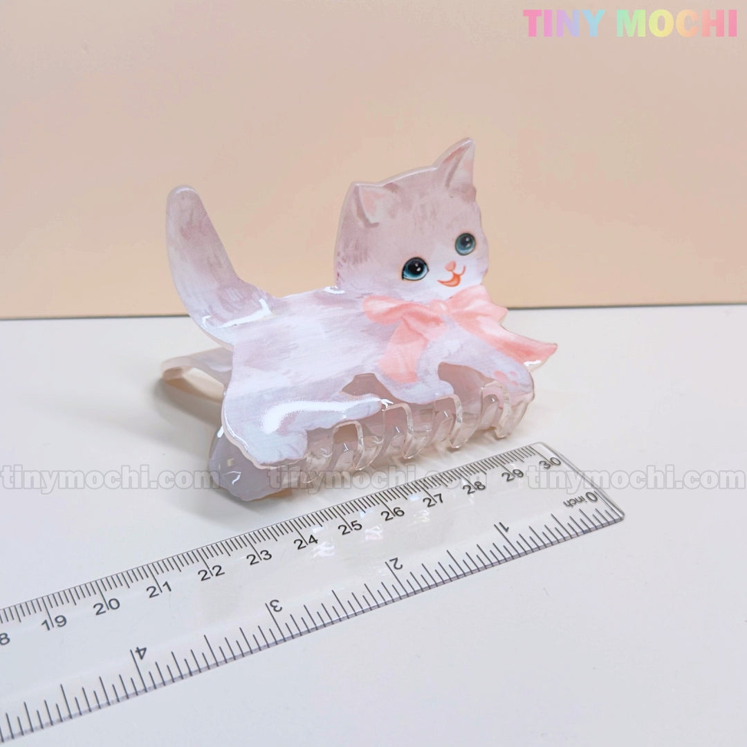 The image shows a light gray cat-shaped Kawaii Dog & Cat Hair Claw Clip with blue eyes and a pink bow by Tiny Mochi, next to a transparent ruler for size. Ideal cute pet-themed hair accessory for girls!.