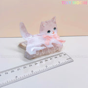 The image shows a light gray cat-shaped Kawaii Dog & Cat Hair Claw Clip with blue eyes and a pink bow by Tiny Mochi, next to a transparent ruler for size. Ideal cute pet-themed hair accessory for girls!.