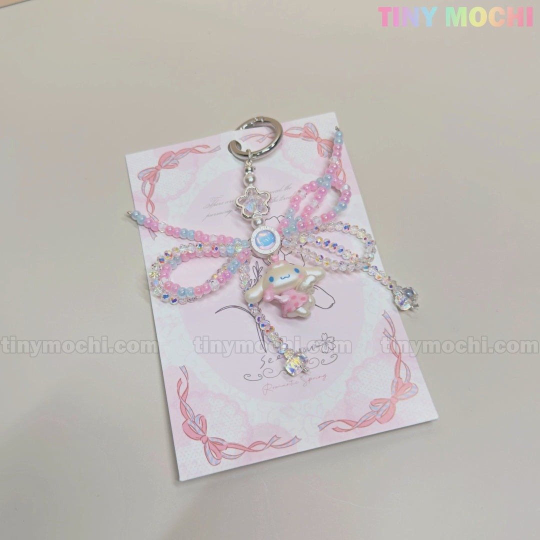 The Cotton Candy Wings Charm Keychain by Tiny Mochi features kawaii pastel beads, a cute Cinnamoroll charm, pink and blue bows, and star accents in fairycore style, displayed on a pink card with the brand name in colorful letters.