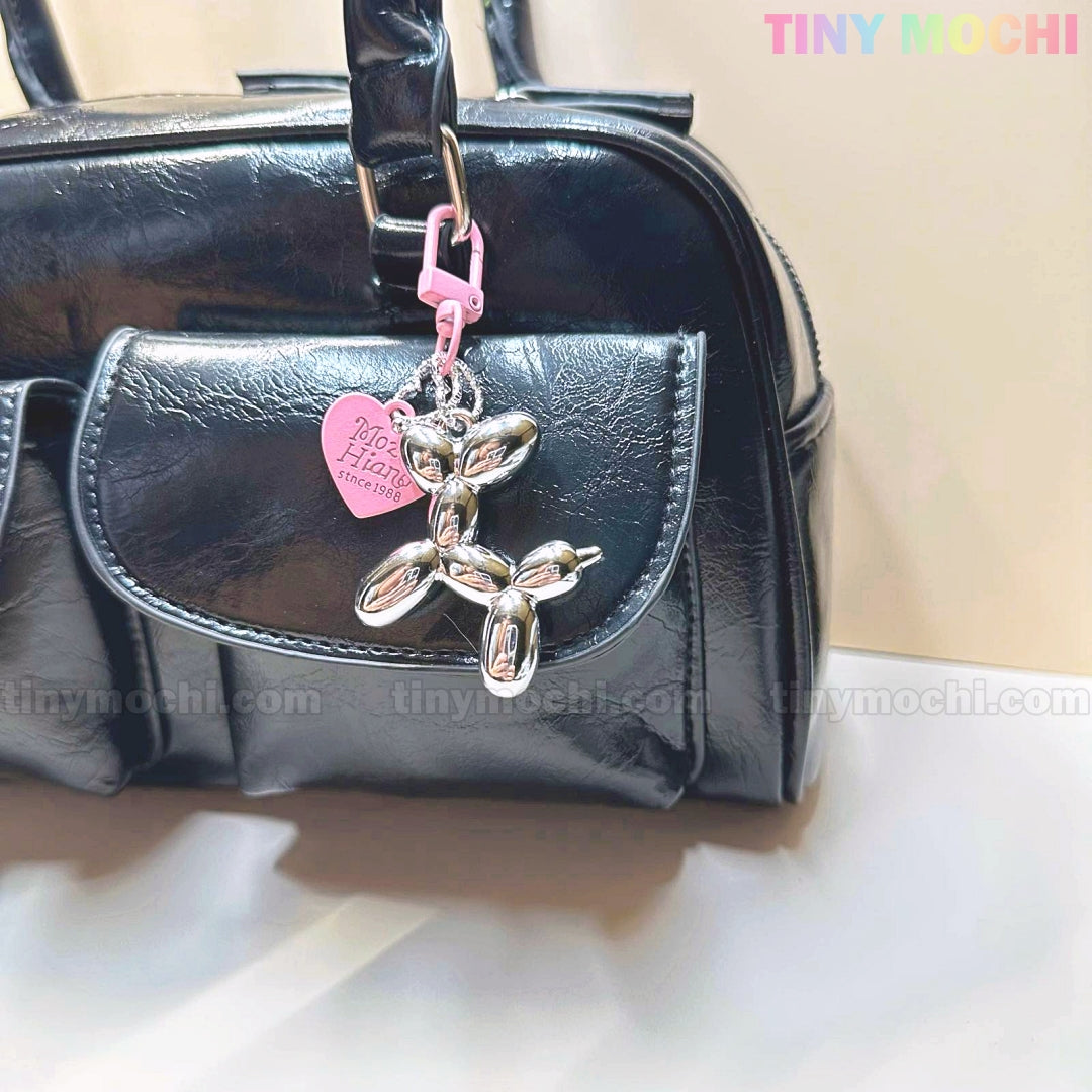 A sleek black handbag features a chrome silver Balloon Dog Keychain bag charm with a pink heart tag, adding cute Y2K flair. The brand name Tiny Mochi is displayed in pastel colors in the top right corner.