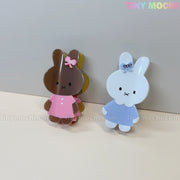 Two adorable Kawaii Bunny Hair Claw Clips by Tiny Mochi—one brown in a pink dress and bow, one white in blue—made from pastel acrylic. Perfect for fans of cute bunnies and pastel hair accessories!.