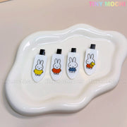 Four Kawaii Bunny Hair Clips for Girls by Tiny Mochi, featuring cute cartoon resin bunnies in colorful outfits and poses on a white wavy dish. Light beige background with TINY MOCHI in pastel colors at the top right.