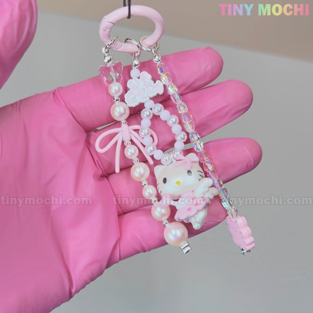 A hand in pink gloves holds the Kawaii Pink Pearl Keychain by Tiny Mochi, featuring a sweet white kitty angel charm, pink bow, pearl and crystal beads, with a pastel neutral background and the brand’s playful label.