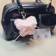 A black handbag styled with Tiny Mochi’s Plush Butterfly Bow Keychain—pink, fuzzy, coquette-inspired, and kawaii—sits beside a Tiny Mochi business card.