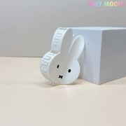 The Kawaii Bunny Face Hair Clip – White Rabbit Claw Clip by Tiny Mochi features a cute bunny face with black eyes and nose, resting against a white box on a cream surface—an adorable kawaii hair accessory.