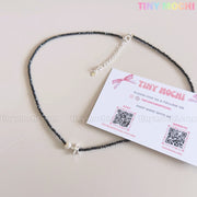 The Sterling Silver Starfish Necklace by Tiny Mochi—a handmade 925 silver charm on a black beaded pearl choker—rests next to a Tiny Mochi card displaying social media and website info on a light pink background.