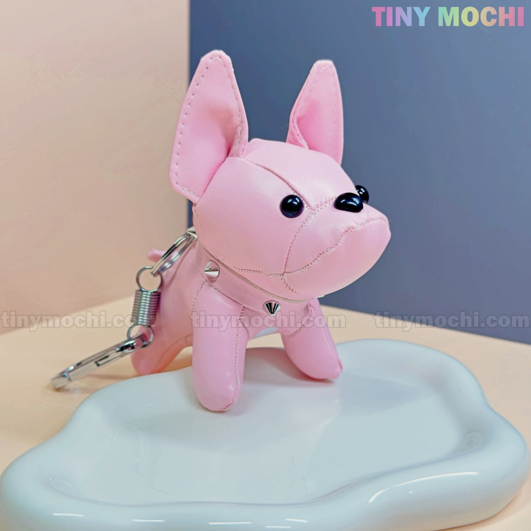 A pink French Bulldog Keychain Coin Purse by Tiny Mochi, featuring large ears and black button eyes, rests on a glossy white surface. “TINY MOCHI” appears in pastel at the top right—a cute faux leather dog bag charm gift for dog lovers.
