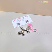 The Tiny Mochi Balloon Dog Keychain Chrome Silver Bag Charm, featuring a cute pink heart tag, shines on a light surface next to a business card. The pastel Tiny Mochi logo appears at the top right.