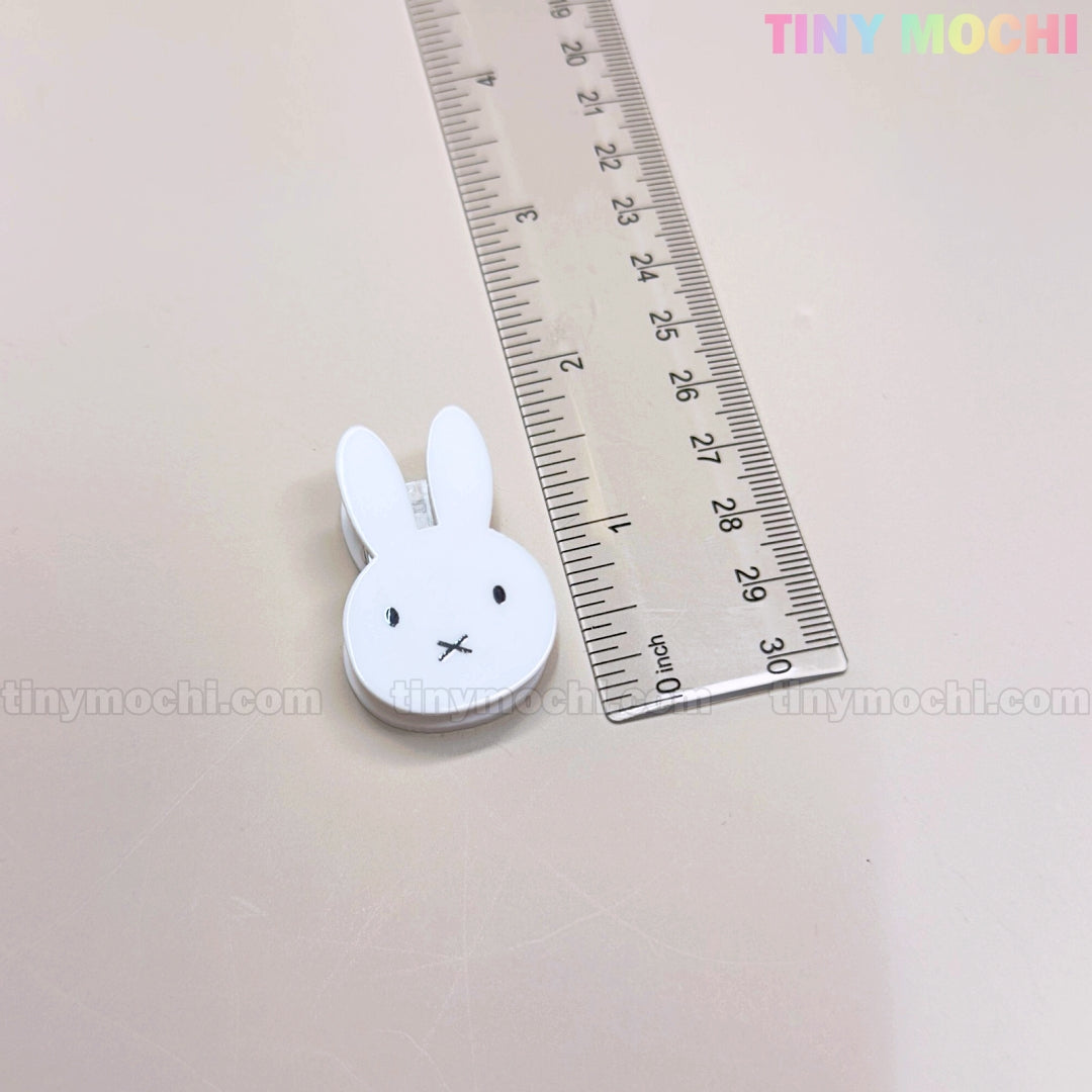 A clear ruler lies next to the Kawaii Bunny Paper Clip by Tiny Mochi, a cute Miffy-inspired white bunny face clip with black eyes, an x mouth, and TINY MOCHI in colorful letters—perfect desk decor and stationery accessory.