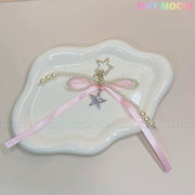 The Pink Star Bow Charm Keychain by Tiny Mochi, with Y2K ribbon, pearls, and silver star details, is shown on a white wavy dish—a kawaii coquette bag or phone accessory. TINYMICHI.COM is subtly visible.