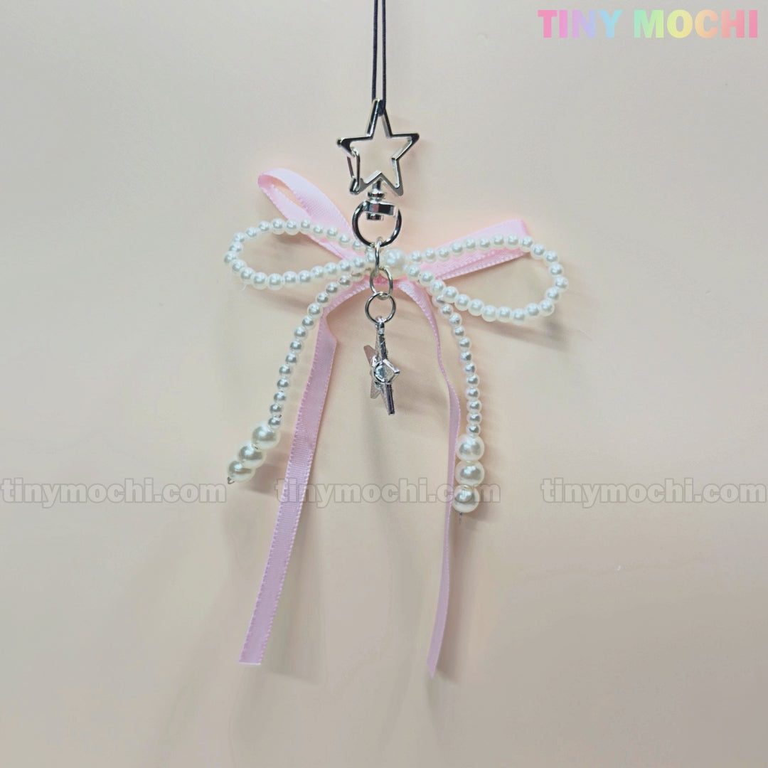 The Pink Star Bow Charm Keychain by Tiny Mochi features a pastel pink ribbon with pearls, silver star pendant clip, and wand charm—an adorable kawaii Y2K accessory for your phone or bag!.