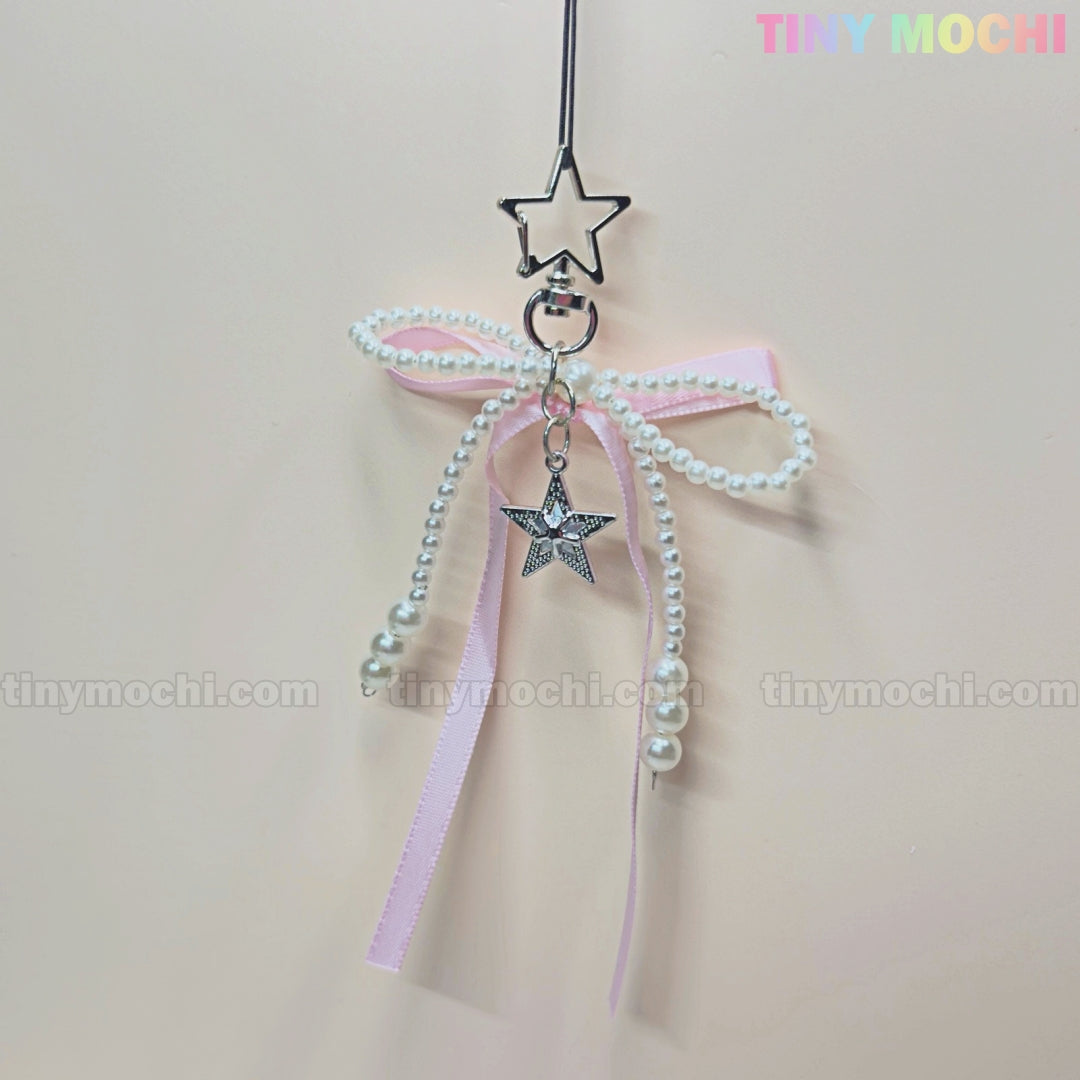 The Pink Star Bow Charm Keychain by Tiny Mochi features a star-shaped clip, pink ribbon bow, faux pearl strands, and a silver star pendant—ideal as a kawaii Y2K phone charm or coquette bag accessory gift.