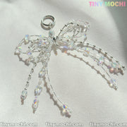 The Tiny Mochi Crystal Bow Pearl Keychain, crafted with clear iridescent beads and silver wire, sparkles on a light textured surface—an aesthetic accessory perfect for bags, keys, and more.