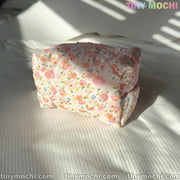 A Tiny Mochi Floral Quilted Cosmetic Bag (6.7 x 4.5 x 3.9) sits on a white, striped fabric in sunlight—perfect as a beauty case or travel pouch. TINY MOCHI appears at the top right and tinymochi.com along the bottom edge.