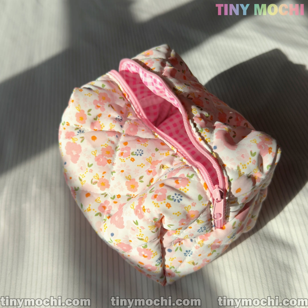 A small Floral Quilted Cosmetic Bag by Tiny Mochi with a pink zipper sits open on a white surface, showing its pink gingham lining. Ideal for travel, this Coquette Quilted Pouch measures 6.7 x 4.5 x 3.9.