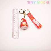 The Tiny Mochi Cute Kawaii Character Keychain features an adorable red and white 3D anime design with a bear charm, Happy Party strap, and gold keyring—shown beside a 15 cm ruler. Perfect for decorating bags or keys!.