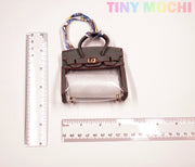 The Tote-Shaped Transparent Key Pouch by Tiny Mochi, a stylish mini bag key holder with gray trim, is shown between two rulers for scale. TINY MOCHI appears in pastel colors at the top right.