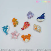 Eight cute sea creature hair clips from Tiny Mochi, featuring mini ocean-themed animal designs like a shark and whale, are arranged in a circle—perfect accessories for pairing with other sea animal hair claws.