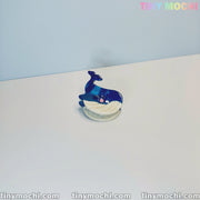 A small, blue and white whale figurine with a smiling face sits on a white surface. Tiny Mochi’s Cute Sea Creature Hair Clips—mini ocean-themed animal acetate hair claws for women & girls—are available now at tinymochi.com.
