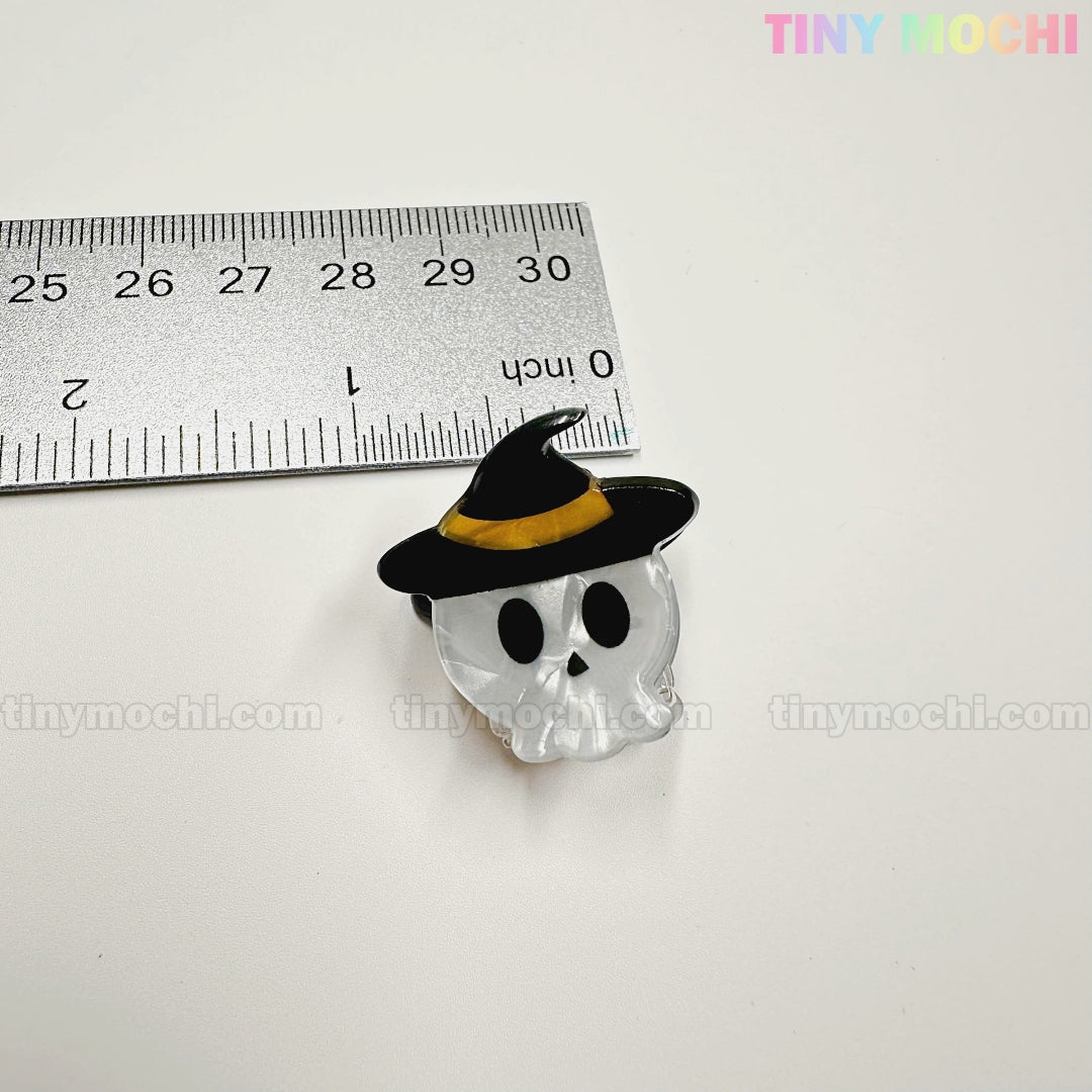 A skull-shaped pin with black eyes and nose and a witch hat sits beside a ruler for scale. From Tiny Mochi Gift Shop Houston’s Kawaii Halloween Hair Claw Clips – Set of 8 Spooky-Cute Designs, perfect for kawaii accessory lovers.