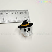 A skull-shaped pin with black eyes and nose and a witch hat sits beside a ruler for scale. From Tiny Mochi Gift Shop Houston’s Kawaii Halloween Hair Claw Clips – Set of 8 Spooky-Cute Designs, perfect for kawaii accessory lovers.