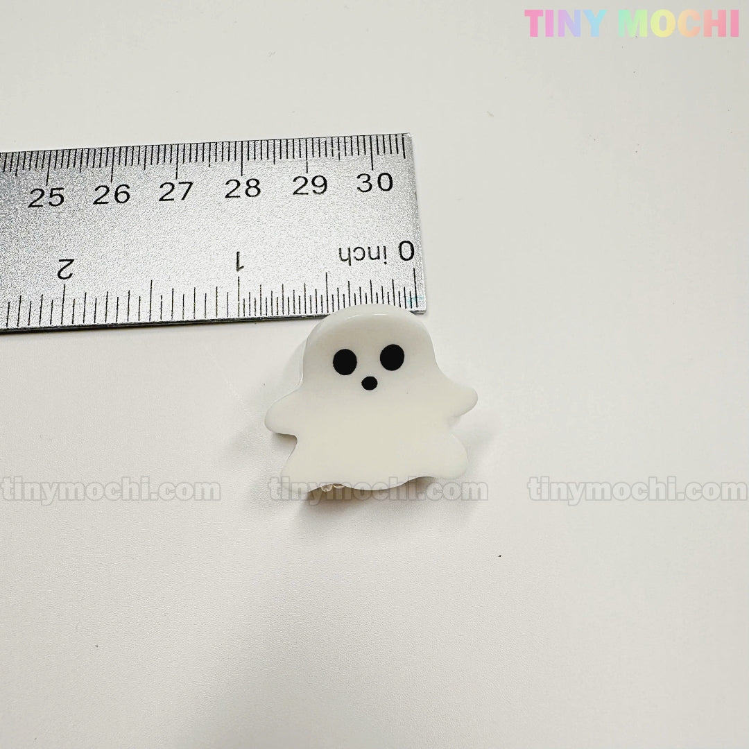 A metal ruler shows a ghost-shaped claw clip, about 1.5 inches tall, from Tiny Mochi Gift Shop Houston’s Kawaii Halloween Hair Claw Clips – Set of 8 Spooky-Cute Designs. Add charm to your hair accessories collection!.