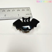 A shiny black bat-shaped Kawaii Halloween Mini Claw Clip by Tiny Mochi Gift Shop Houston sits next to a silver ruler on a white background with "TINYMochi.com" faintly visible. Perfect spooky cute hair accessory for Halloween!.