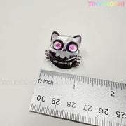 A small, purple cat-shaped keycap with a skull face sits by a metal ruler measuring about 1 inch wide. "TINY MOCHI" appears in pastels—perfect for fans of the Kawaii Halloween Mini Claw Clips from Tiny Mochi Gift Shop Houston.