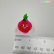 A small, pink, onion-shaped charm with a smiling face and green top sits by a ruler showing it's about 3 cm wide. From the Kawaii Vegetable Hair Clip Set – 8 Pieces by Tiny Mochi Gift Shop Houston. Light gray background with pastel TINY MOCHI branding.