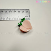 A small, peach-shaped pin from the Fruity Friends Hair Clip Set by Tiny Mochi Gift Shop Houston is shown next to a ruler (about 1 inch wide). The light background has a faint tinymochi.com watermark. Perfect for cute, fruity hair accessories!.