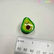 A cute, 1-inch avocado-shaped hair clip from the Fruity Friends Hair Clip Set by Tiny Mochi Gift Shop Houston sits on a white surface next to a ruler. Perfect kawaii accessory for kids' hair or collections! "TINY MOCHI" appears in the corners.