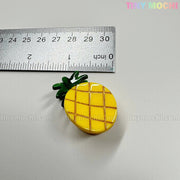 A small yellow pineapple-shaped hair clip from the Fruity Friends Hair Clip Set by Tiny Mochi Gift Shop Houston is shown next to a metal ruler, measuring about 3cm long. "TINY MOCHI" appears in colorful text in the top right corner.