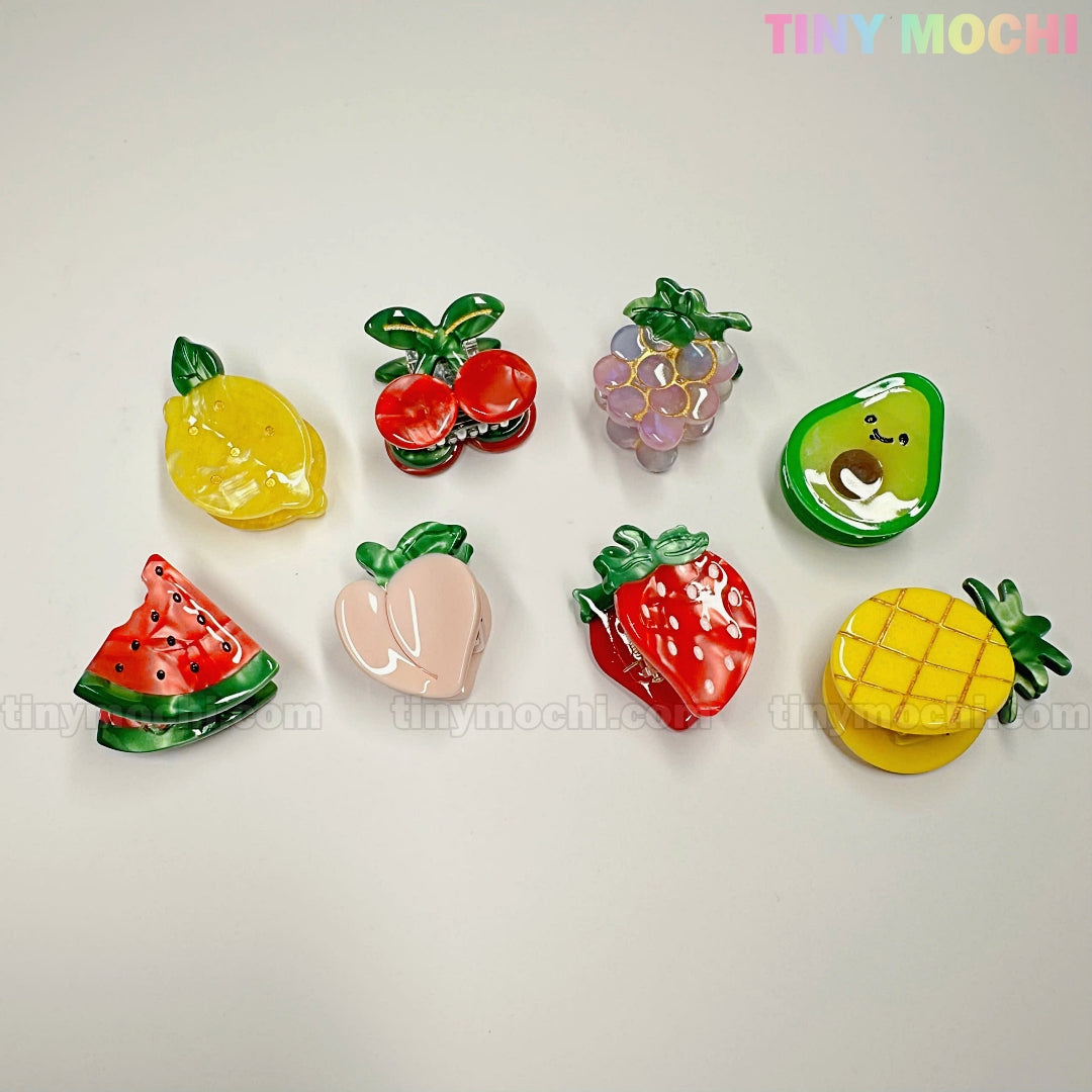 The Fruity Friends Hair Clip Set from Tiny Mochi Gift Shop Houston features eight colorful fruity hair clips, including lemon, cherry, and avocado, arranged on a light background in adorable pastel shades.